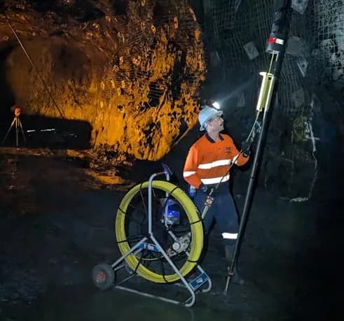 Surveyor underground pushing the gyro up a hole on the Feeder Pole, rodder reel at their feet